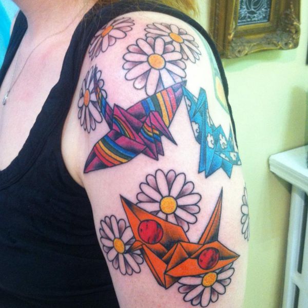 Gänseblümchen und Origami Kranich Tattoo am Oberarm